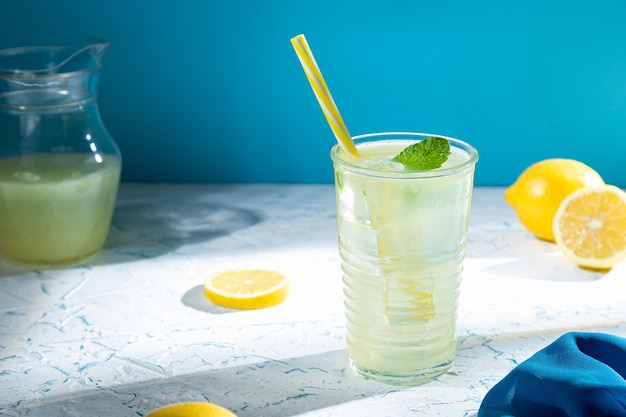 Vetro con limonata e limoni su sfondo blu chiaro.