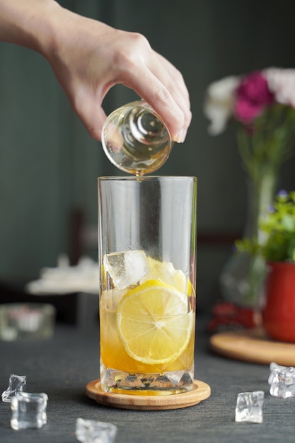 Vetro con succo di limone e limone fresco a fette sul tavolo in legno e copia spazio, cocktail estivo, caffè freddo o tè nero. (primo piano, fuoco selettivo), versando la bevanda fredda.