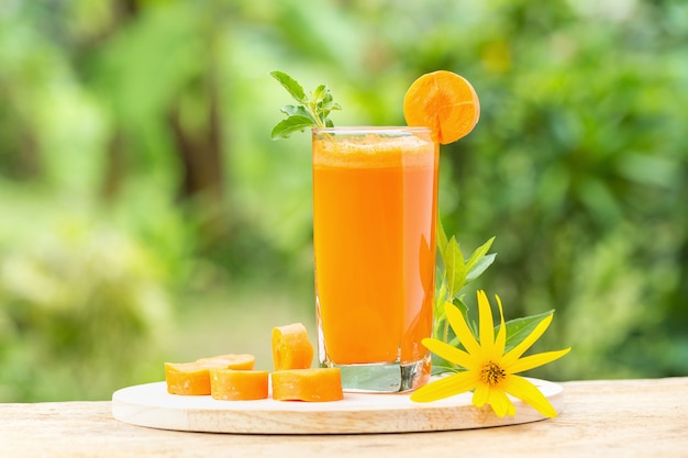 Vetro del succo di carota e delle carote fresche su un fondo di legno con il backgroun di verde della natura