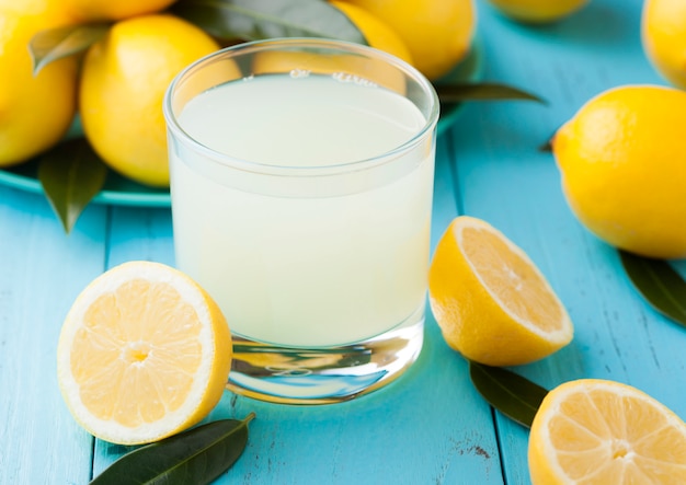 Vetro del succo di limone fresco organico con i limoni crudi su di legno blu