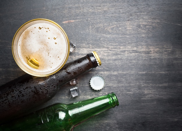 Vetro di birra con tappo di bottiglia e bottiglia su fondo di legno rustico, spazio per testo, vista dall&#39;alto