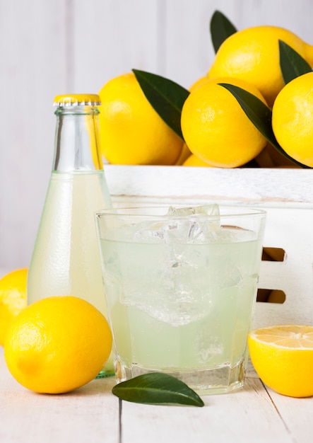 Vetro e bottiglia del succo di limone fresco organico con i limoni crudi in scatola di legno bianca