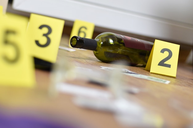 Vetro rotto e bottiglia di vino contrassegnati come prove durante le indagini sulla scena del crimine. Molti marcatori gialli con numeri