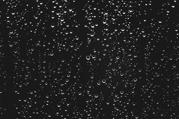 Vetro sporco della finestra con le gocce di pioggia. Atmosfera monocromatica scura con gocce di pioggia. Goccioline e macchie si chiudono. Struttura trasparente dettagliata nella macro con copyspace. Tempo piovoso.