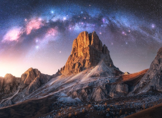 Via Lattea acrh su bellissime rocce di notte stellata in estate nelle Dolomiti Italia Paesaggio con cielo viola con stelle e luminosa via lattea arcuata su alte montagne rocciose alpine Spazio Natura