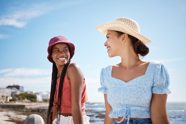 Viaggi estivi e amiche in spiaggia per rilassarsi con la moda del cappello da sole godendo le vacanze Amicizia delle giovani donne con la donna nera e la signora latina che si godono il sole delle vacanze sull'oceano insieme