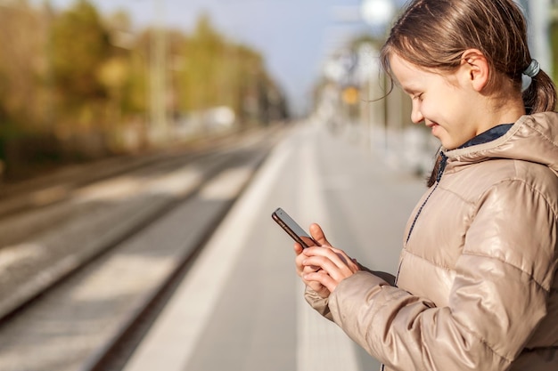 Viaggi in app per dispositivi mobili. La ragazza felice ha usato lo Smart phone sulla stazione ferroviaria. App mobile nel telefono per i viaggi.