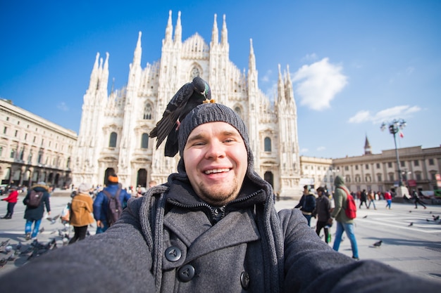 Viaggi invernali, vacanze e concetto di uccelli - Giovane uomo divertente che si fa selfie con i piccioni vicino al Duomo di Milano Duomo di Milano, Italia.