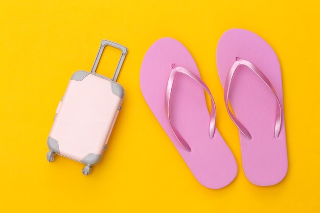 Viaggi o resort sulla spiaggia distesi. Mini valigia da viaggio in plastica e infradito su sfondo giallo. Stile minimale. Vista dall'alto