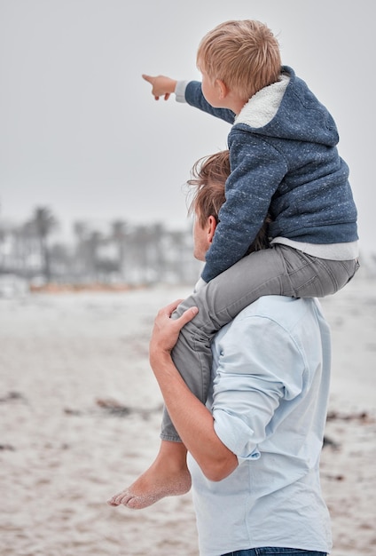 Viaggia con la famiglia e il padre con il figlio in spiaggia divertendosi mentre si porta il bambino sulle spalle e si gode la vista in Messico Genitore e mano del ragazzo che indicano il cielo nuvoloso durante una vacanza al mare