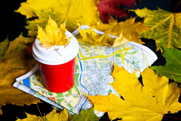 Viaggia in autunno. Caffè per andare, foglie, mappa su sfondo nero