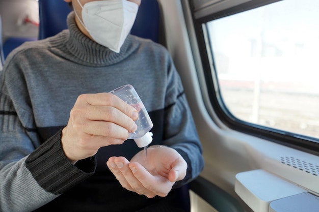 Viaggia in sicurezza sui mezzi pubblici Giovane uomo con maschera protettiva utilizzando dispenser di gel disinfettante per le mani di lavaggio Passeggero con maschera medica disinfetta le mani nel vagone del treno