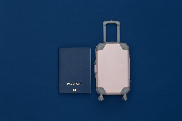 Viaggia piatto. Mini valigia da viaggio in plastica, passaporto su sfondo blu classico. Stile minimale. Vista dall'alto