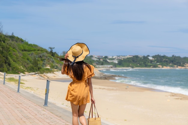 Viaggiare donna con cappello di paglia e camminare lungo la spiaggia di sabbia