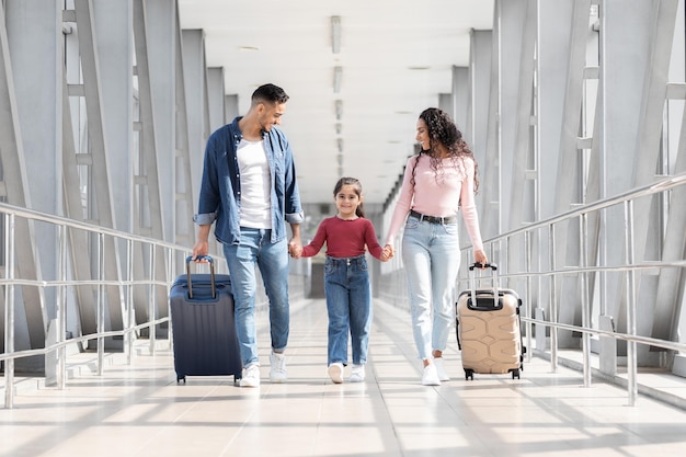 Viaggiare insieme gioiosa famiglia araba che cammina con le valigie al terminal dell'aeroporto