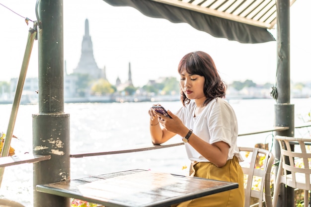 Viaggiatore asiatico della donna che utilizza il suo telefono nel caffè