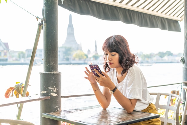Viaggiatore asiatico della donna che utilizza il suo telefono nel caffè