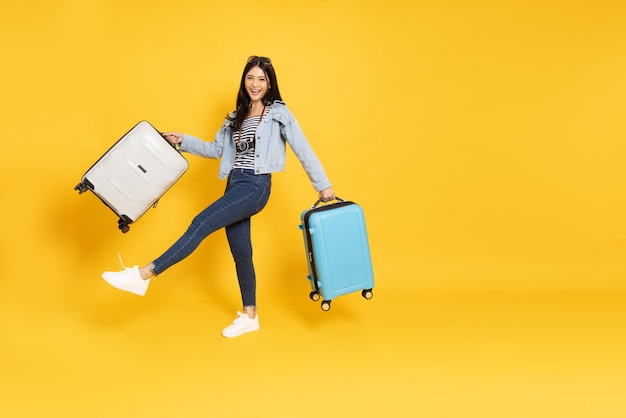 Viaggiatore asiatico felice della donna che sta e che tiene la valigia isolata su fondo giallo