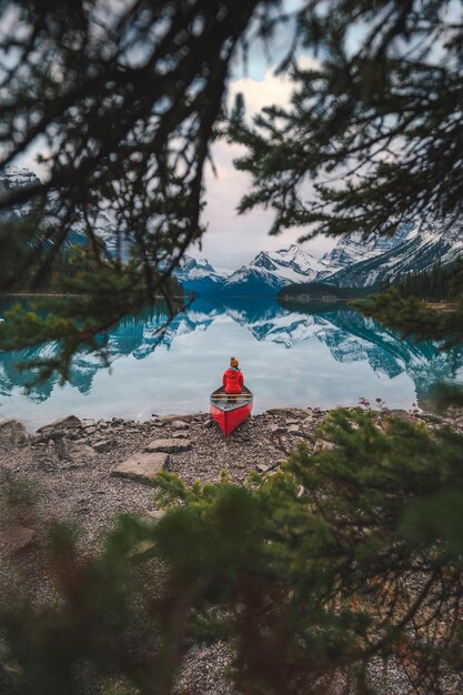 Viaggiatore asiatico in giacca rossa seduto su una canoa in riva al lago a Spirit Island, situato nel lago Maligne nel parco nazionale di Jasper