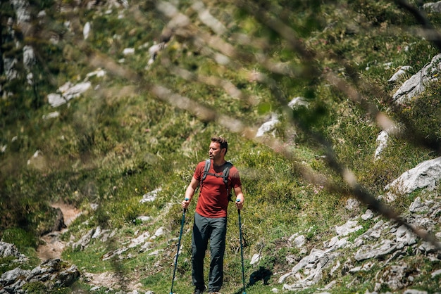 Viaggiatore barbuto serio con zaino appoggiato su bastoncini da trekking mentre esplora gli altopiani