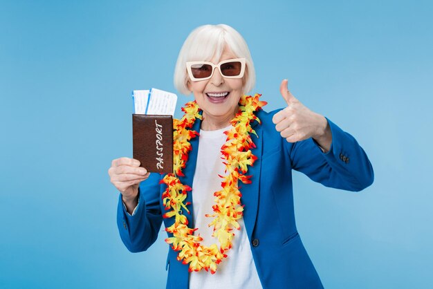 Viaggiatore caucasico maturo della donna che mostra il pollice in su in occhiali da sole che tengono il passaporto ed i biglietti