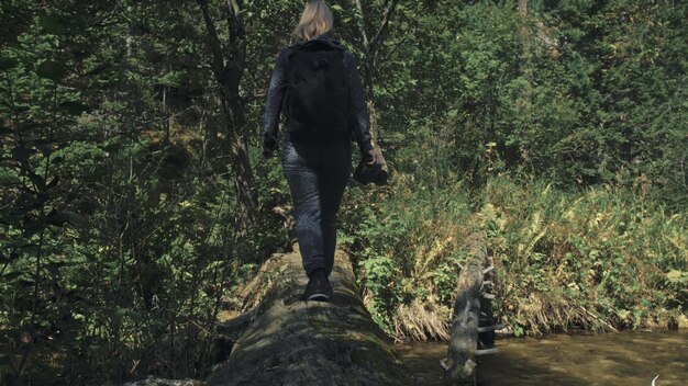 Viaggiatore che fotografa la vista panoramica nel fiume della foresta Albero caduto ponte di legno Una donna caucasica che spara un bel look magico Ragazza scatta foto video sulla fotocamera Il fotografo viaggia con lo zaino All'aperto