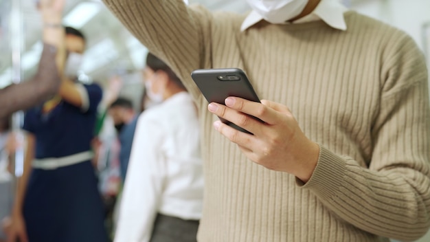 Viaggiatore che indossa la maschera mentre utilizza il telefono cellulare sul treno pubblico