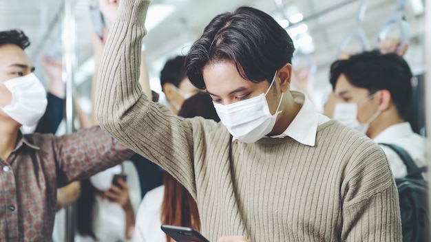 Viaggiatore che indossa la maschera per il viso mentre si utilizza il telefono cellulare sul treno pubblico