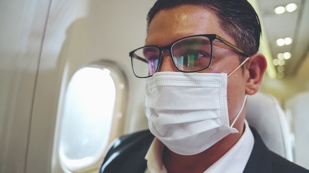 Viaggiatore che indossa una maschera facciale durante il viaggio in aereo commerciale.