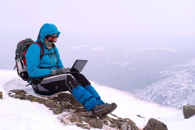 Viaggiatore che lavora con un laptop in inverno in cima a una montagna durante la tempesta di neve