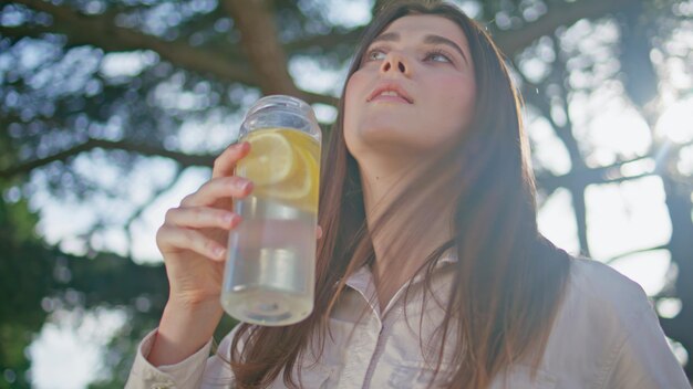 Viaggiatore che rifornisce l'acqua nel parco estivo close-up femmina che beve bevanda al limone