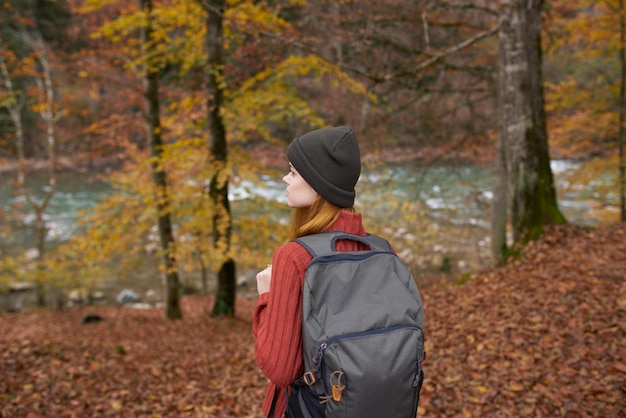 Viaggiatore con uno zaino e in un cappello grigio nella foresta di autunno foglie cadute alberi modello fiume