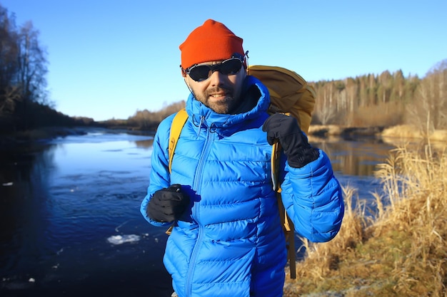 viaggiatore con uno zaino in riva al fiume / ragazzo turistico durante un'escursione nel nord, viaggio invernale