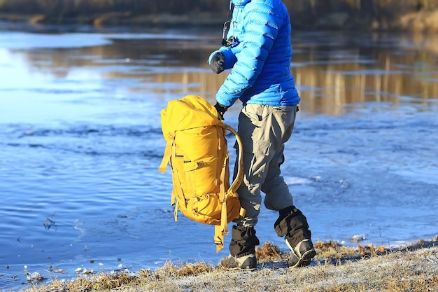 viaggiatore con uno zaino in riva al fiume / ragazzo turistico durante un'escursione nel nord, viaggio invernale