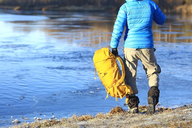 viaggiatore con uno zaino in riva al fiume / ragazzo turistico durante un'escursione nel nord, viaggio invernale