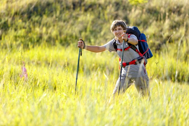 Viaggiatore con zaino e bastoncini da trekking. Il viaggiatore della donna passa attraverso l'erba alta. Fotografato in Russia.