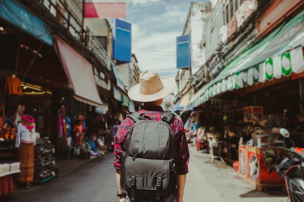 Viaggiatore con zaino e sacco a pelo di viaggio del giovane con il cappello che cammina in via di camminata.