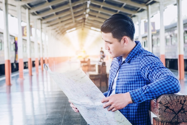 Viaggiatore con zaino e sacco a pelo turistico che utilizza la mappa per viaggiare alla stazione ferroviaria