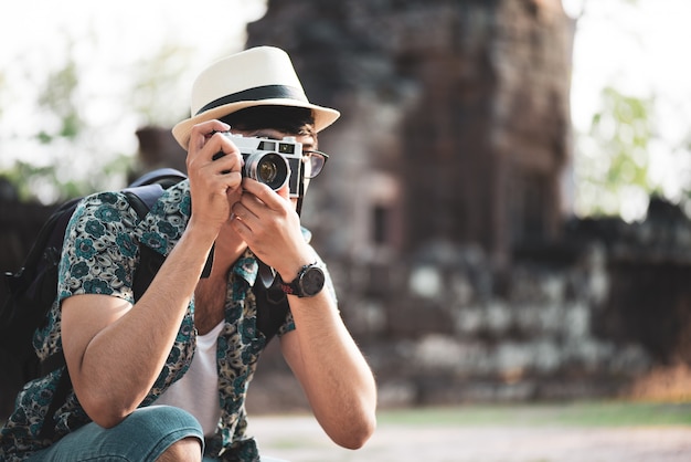 Viaggiatore del fotografo del giovane con lo zaino che cattura foto con la sua macchina fotografica