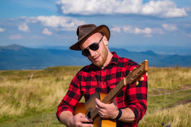 Viaggiatore del giovane in vacanza in campeggio con la chitarra rilassante all'aperto con le montagne durante le vacanze estive l