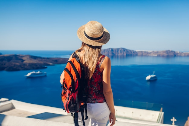 Viaggiatore della donna che esamina caldera da Fira o Thera, isola di Santorini, Grecia. Turismo, viaggi, concetto di vacanza