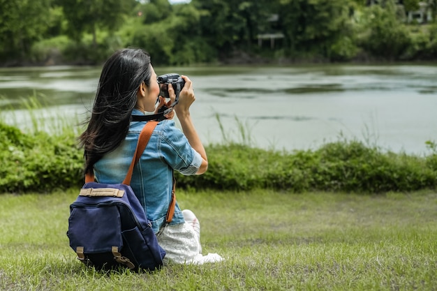 Viaggiatore della donna che si siede sull&#39;erba e che prende la vista della foto della diga