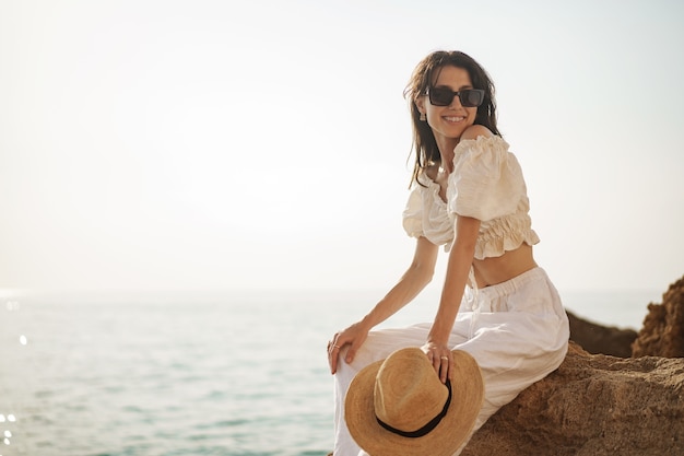 Viaggiatore della donna che si siede vicino al mare sulla scogliera che gode della vista del mare e della natura