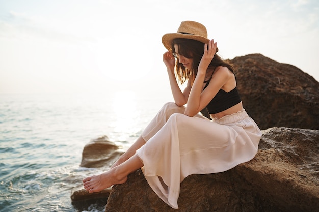 Viaggiatore della donna che si siede vicino al mare sulla scogliera che gode della vista del mare e della natura