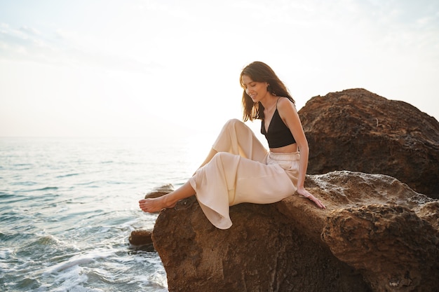 Viaggiatore della donna che si siede vicino al mare sulla scogliera che gode della vista del mare e della natura