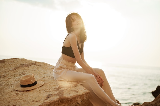 Viaggiatore della donna che si siede vicino al mare sulla scogliera che gode della vista del mare e della natura