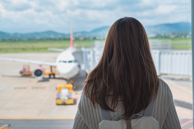 Viaggiatore della giovane donna che esamina l'aeroplano all'aeroporto