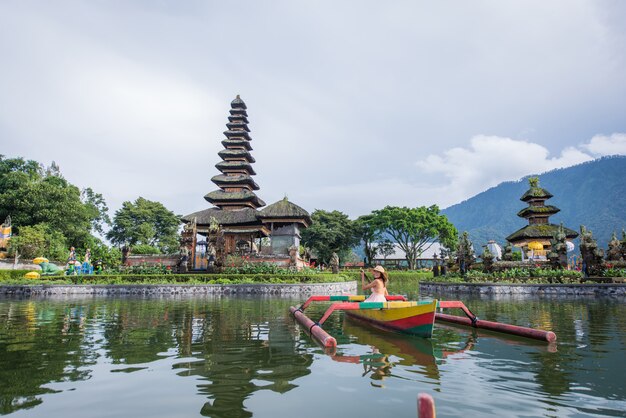 Viaggiatore della giovane donna che rema su una barca di legno a Pura Ulun Danu Bratan