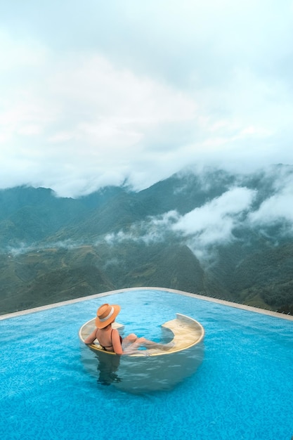 Viaggiatore della giovane donna che si rilassa alla piscina a sfioro con le belle montagne del paesaggio della natura in Sapa Vietnam