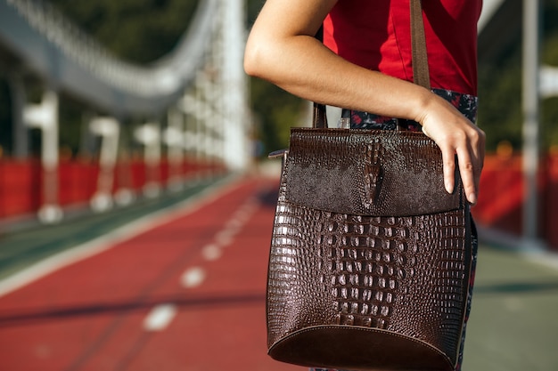 Viaggiatore della giovane donna che tiene la borsa di cuoio che posa al ponte nella giornata di sole. Copia spazio